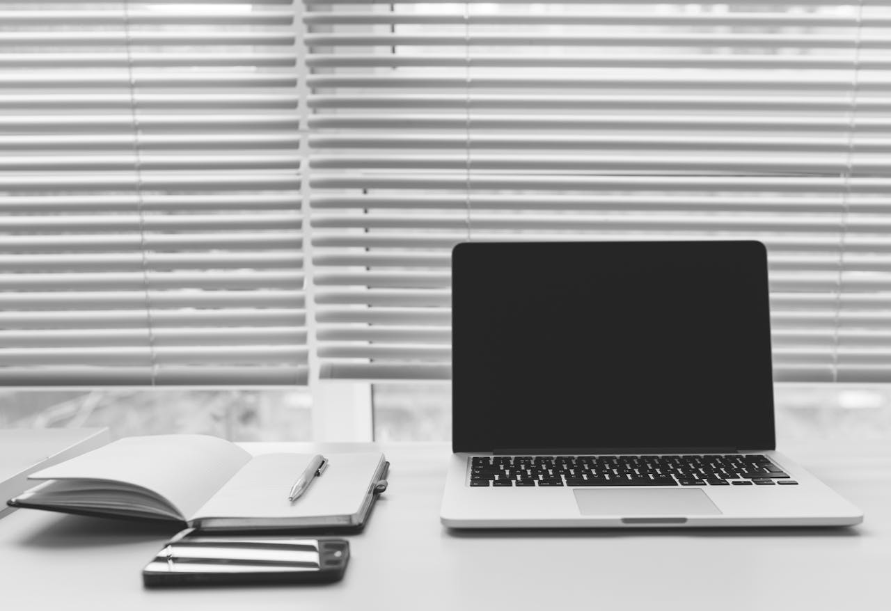 Minimalist black and white workspace featuring a laptop, notebook, and smartphone on a desk.